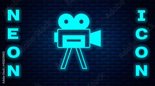 Glowing neon Retro cinema camera icon isolated on brick wall background. Video camera. Movie sign. Film projector. Vector