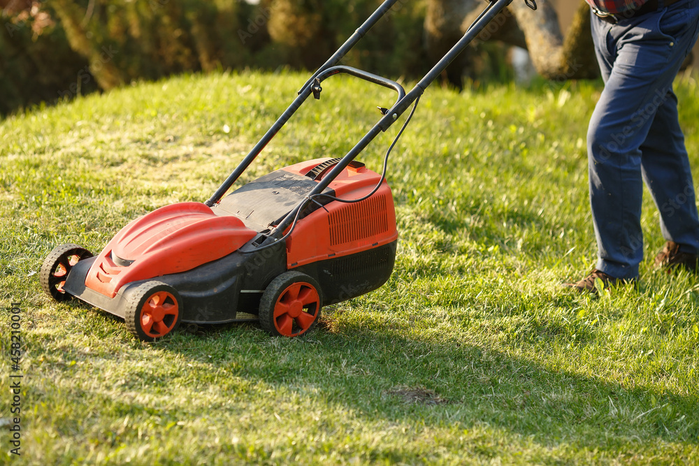 mowing trimmer - worker cutting grass in green yard at sunset. Man with electric lawnmower, lawn mowing. Gardener trimming a garden. mowing trimmer - worker cutting grass in green yard at sunset. Man with electric lawnmower, lawn mowing. Gardener trimming a garden.
