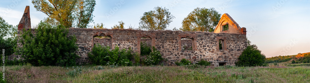 Panorama, old mill overgrown with bushes and grass without windows and a roof. Remains ancient semi collapsed building with stone