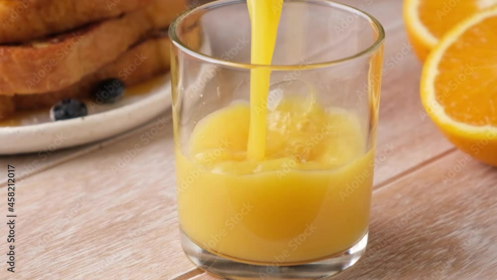 Orange juice pouring in a glass in slow motion, wooden table background. Breakfast concept Orange juice pouring in a glass in slow motion, wooden table background. Breakfast concept