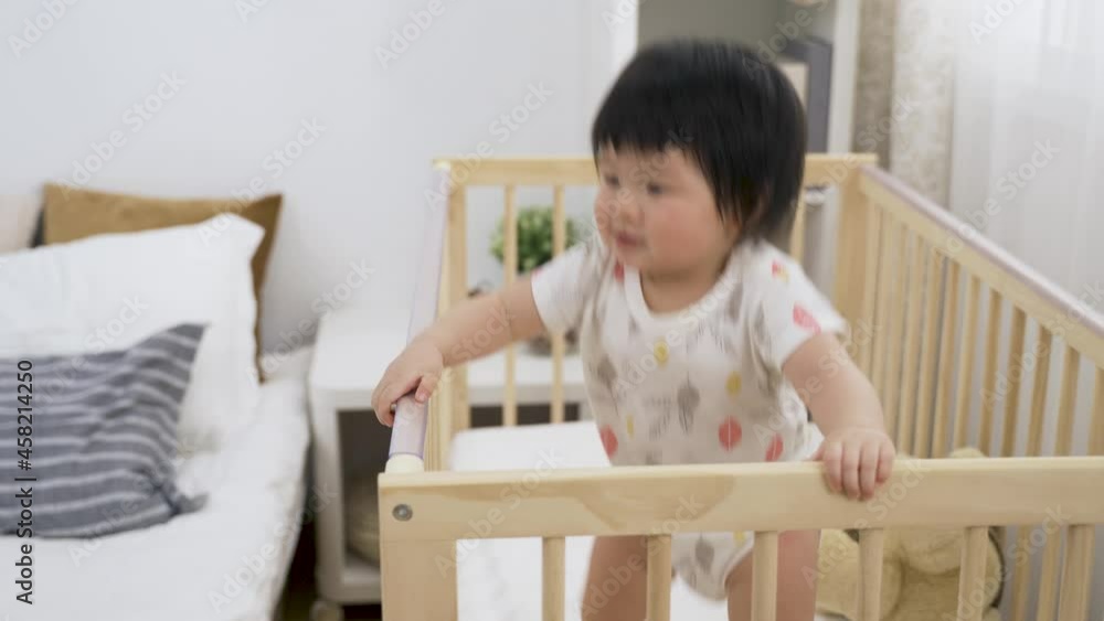 portrait energetic asian young child is gazing into the distance and jumping for joy in the wooden baby crib at a cozy bright home interior. portrait energetic asian young child is gazing into the distance and jumping for joy in the wooden baby crib at a cozy bright home interior.