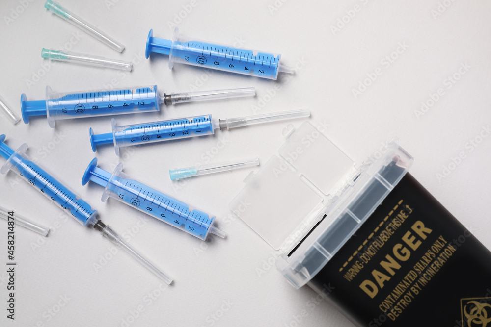 Disposable syringes, needles and sharps container on light background, flat lay Disposable syringes, needles and sharps container on light background, flat lay