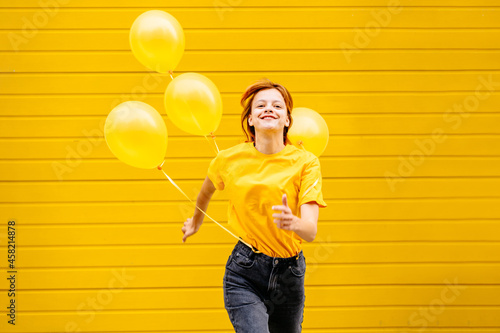 Papier peint Adult hipster girl having fun, jumping and running with helium yellow balloons on yellow background in the city street outdoor