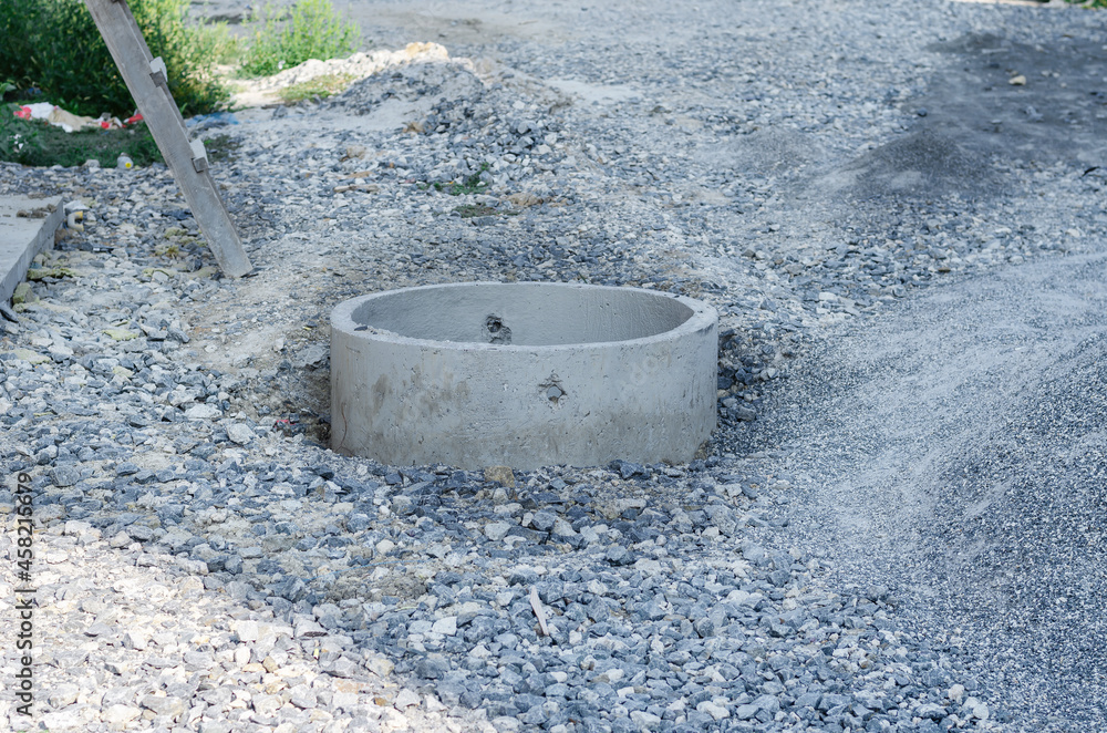 Construction site. Open concrete sewage well among the gravel. Industry. Selective focus.