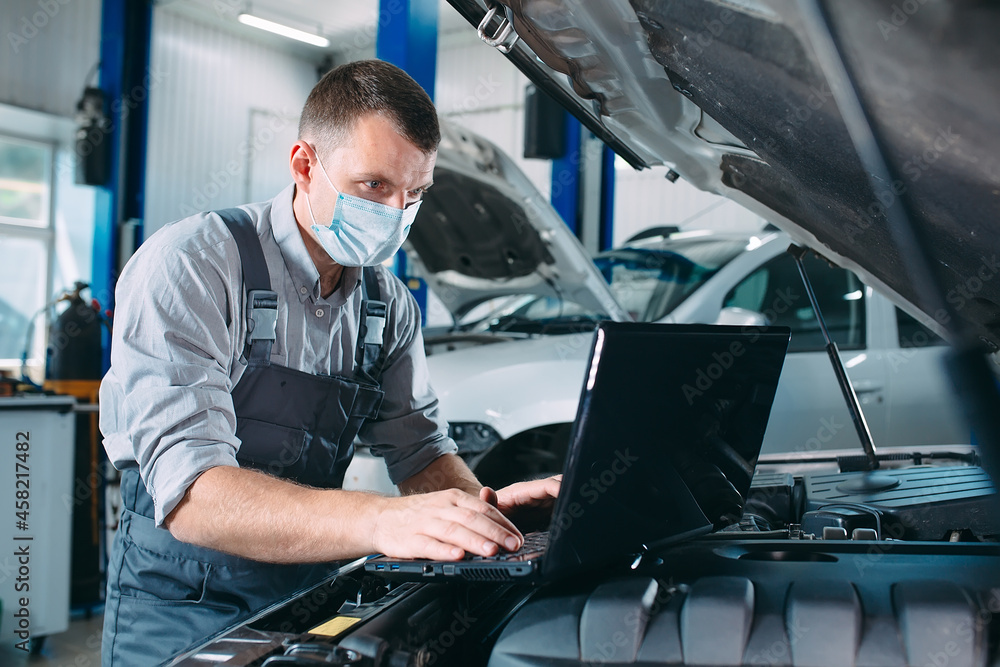 car mechanic using a computer laptop to diagnosing and checking up on car engines parts for fixing and repair. car mechanic using a computer laptop to diagnosing and checking up on car engines parts for fixing and repair.