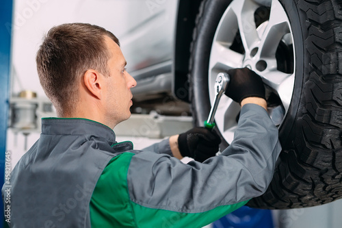 Car lifted in automobile service for fixing, worker repairs the wheel,