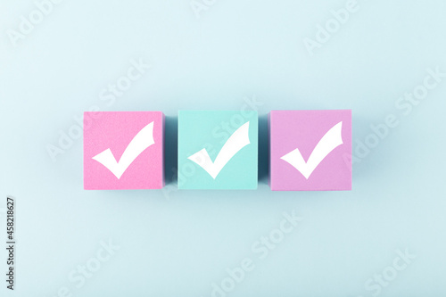 Three checkmarks on multicolored cubes in a row in the middle of bright pastel blue background. Concept of questionary, checklist, to do list, planning, business or verification. Modern minimal compos