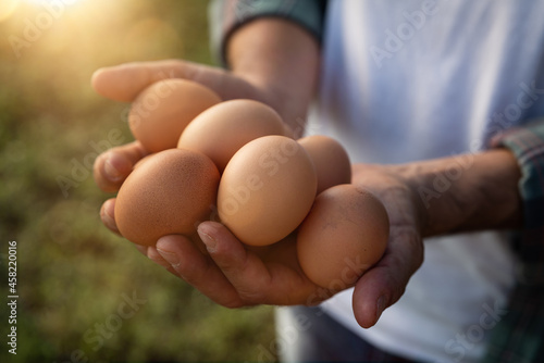 Close up of farmer is showing fresh eggs laid at the moment by ecologically grown hens in barn of countryside agricultural farm. Concept of agriculture, bio and eco farming, bio food products.