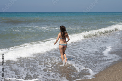 Young woman in a white shirt is bathes in the waves in the sea foam on an exotic tropical island