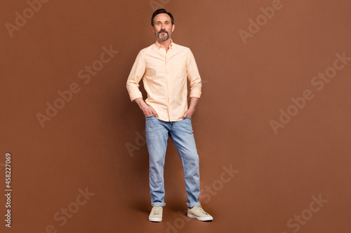 Photo of confident successful businessman hands pockets wear beige shirt jeans isolated brown color background