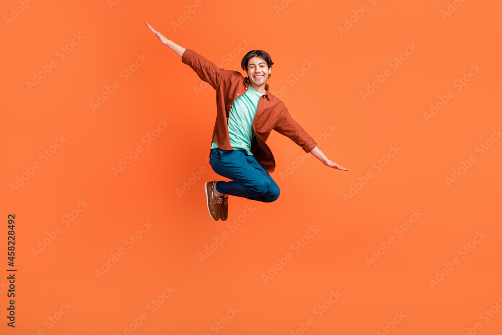 Full size photo of smiling good mood childish guy jumping fooling around carefree isolated on orange color background