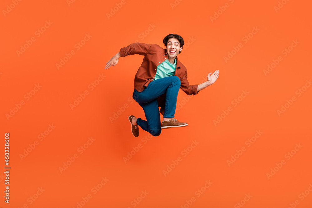 Full size photo of cheerful good mood man running in air traveling wear brown shirt isolated on orange color background