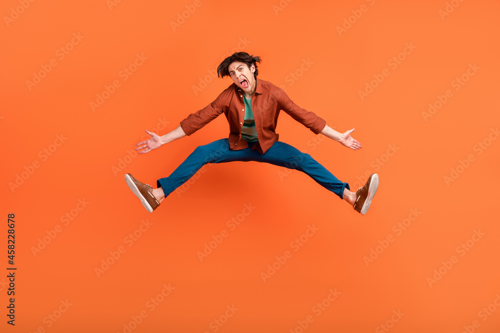 Obraz premium Full size photo of funky funny man jumping unhappy shrug shoulders fooling around isolated on orange color background