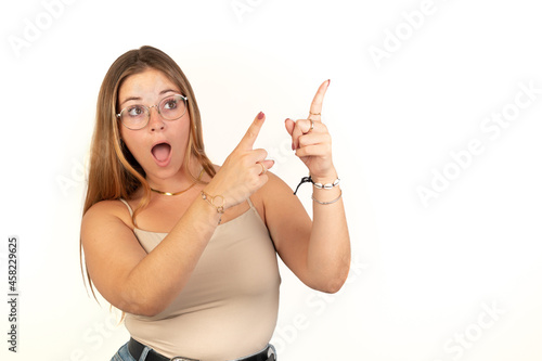 Surprised blonde woman pointing right upper corner with both hands. White background. 20 - 22 years old. White European woman.