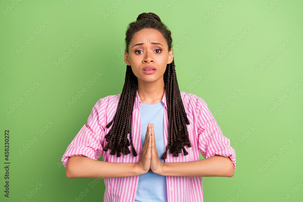 Photo of guilty upset dark skin woman dressed striped shirt arms together asking forgiveness isolated green color background Photo of guilty upset dark skin woman dressed striped shirt arms together asking forgiveness isolated green color background