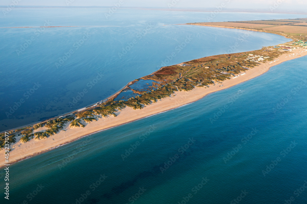 Long spit with sandy beach between sea and liman at sunset, aerial view from drone. Blagoveshchenskaya, Anapa region, Russia.