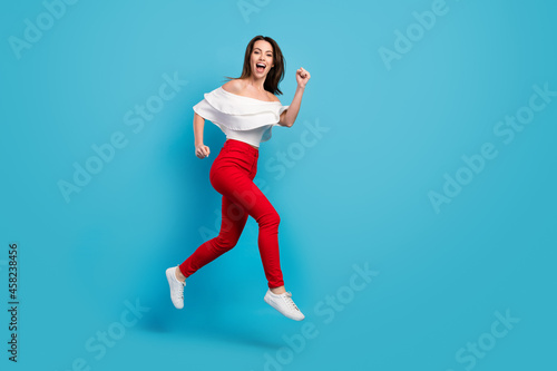 Photo of shiny excited young lady wear off-shoulders shirt jumping high running empty space smiling isolated blue color background