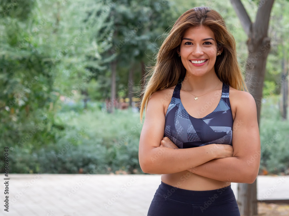 Smiling sporty young woman working out outdoors and looking at camera. Confident Hispanic girl sportswear training. Portrait of happy runner with crossed arms in an urban park. Copy space Smiling sporty young woman working out outdoors and looking at camera. Confident Hispanic girl sportswear training. Portrait of happy runner with crossed arms in an urban park. Copy space