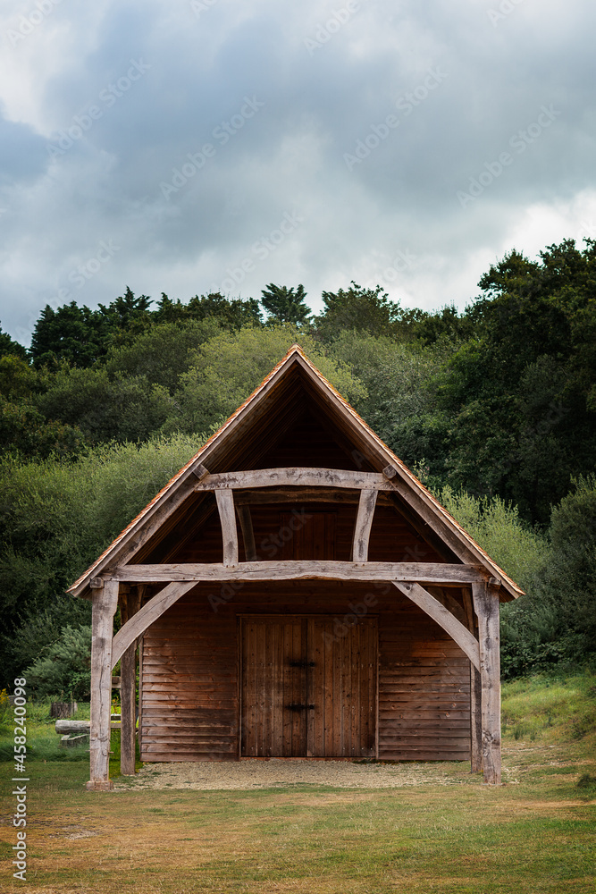 Front on view of barn building with thick wood construction and tiled roof. Forest setting in background with cloudy sky above. Copy space available. Front on view of barn building with thick wood construction and tiled roof. Forest setting in background with cloudy sky above. Copy space available.