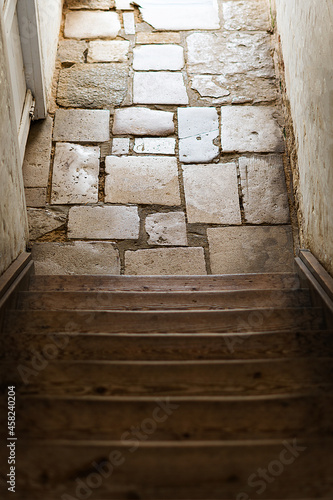 Old worn wooden steps leading down to traditional stone floor and out towards natural daylight. Old interior building in neutral colours and tones. Copy space available.