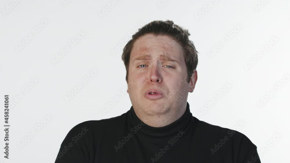 Medium close-up portrait with slowmo of young emotional man crying at camera standing at white background in studio Medium close-up portrait with slowmo of young emotional man crying at camera standing at white background in studio