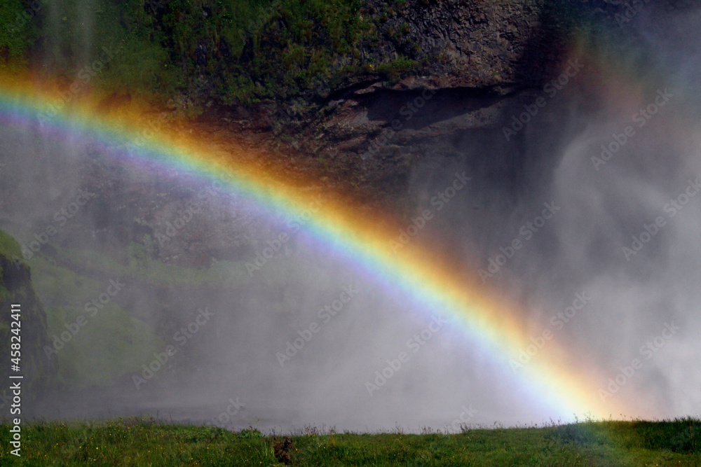 A rainbow in front of Seljalandsfoss waterfall on the southern coast of Iceland on a sunny day