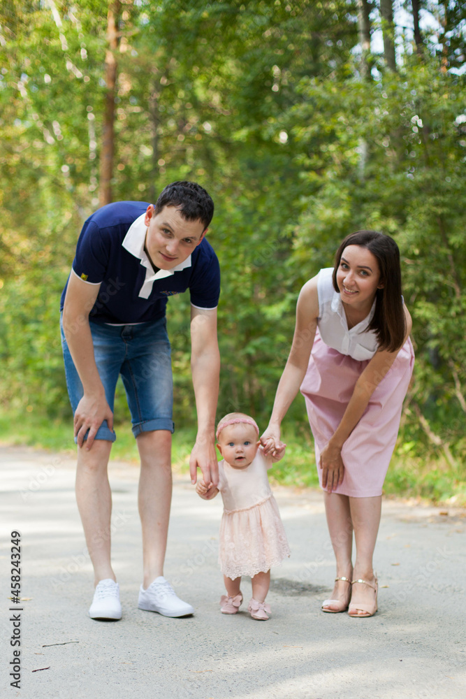 Happy beautiful family on a walk. First steps. Mom, Dad and their little daughter walk by the hand. summer, emotions. Happy beautiful family on a walk. First steps. Mom, Dad and their little daughter walk by the hand. summer, emotions.
