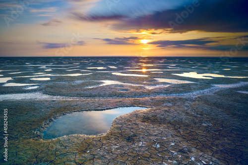 Fotografia Shot of a sea coast spangled by stone with the sunrise reflecting on the wet san