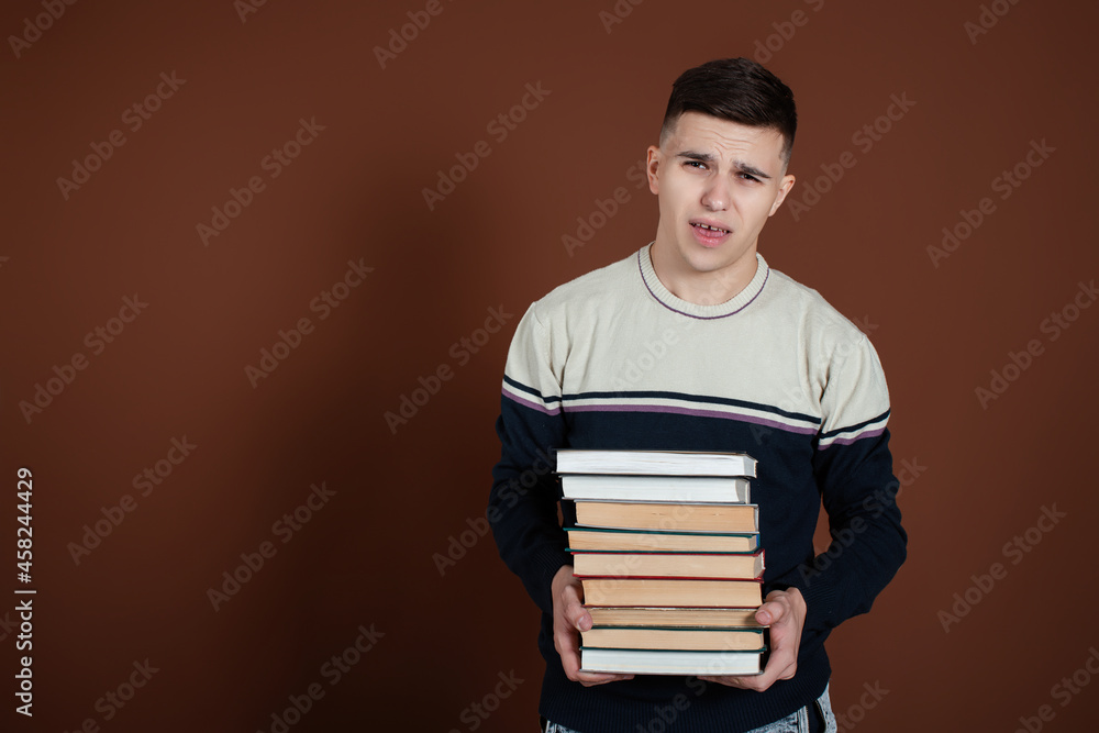 Funny student nerd in glasses with books in hands. Brown background. Preparing for exams in the library. Funny student nerd in glasses with books in hands. Brown background. Preparing for exams in the library.