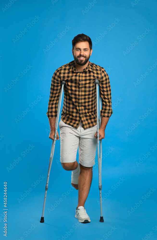 Young man with injured leg using axillary crutches on light blue background Young man with injured leg using axillary crutches on light blue background