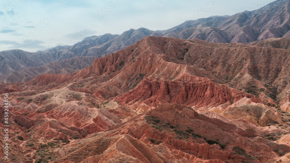 An unusual aerial landscape with huge red brown rocks and a mountain on which a man in a red T-shirt is sitting and meditating. A deserted canyon with gorges filmed on a copter on a sunny day.