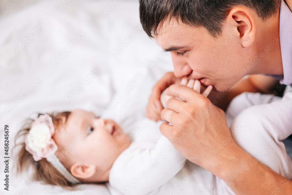 a newborn girl is lying with her young father in a snow-white bed. dad kisses the hands of his newborn daughter. the concept of the family a newborn girl is lying with her young father in a snow-white bed. dad kisses the hands of his newborn daughter. the concept of the family