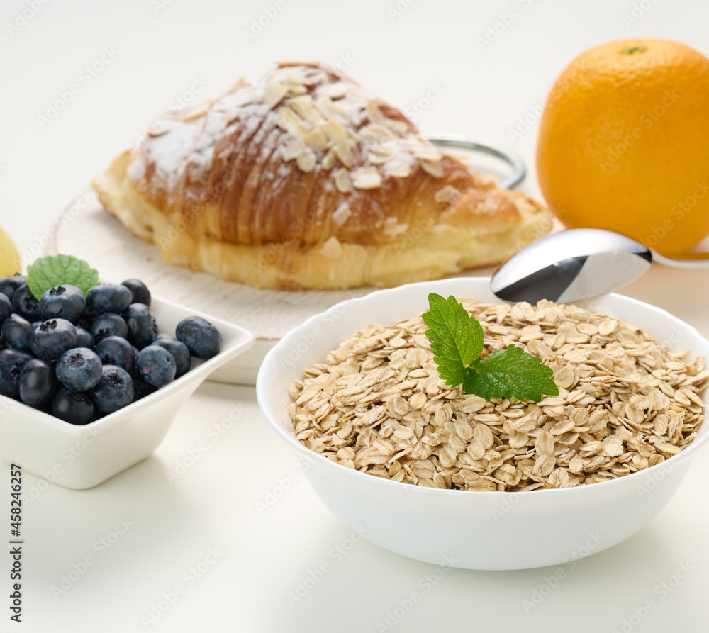 Raw oatmeal in white ceramic plate, blueberry, orange, on white table, Raw oatmeal in white ceramic plate, blueberry, orange, on white table,