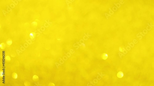 Festive yellow glitter background with moving and flicker particles. Magic dust, shiny texture and holiday lights, flying particles with beautiful bokeh. Shining christmas backdrop
