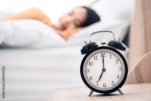 Young woman sleeping on bed with alarm clock in morning.