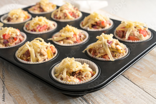 Prepared pizza muffins from yeast dough with tomatoes, vegetables and cheese in a baking tray ready for the oven, selected focus