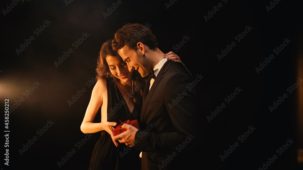 happy young man in suit with bow tie giving red present to woman in dress on black happy young man in suit with bow tie giving red present to woman in dress on black