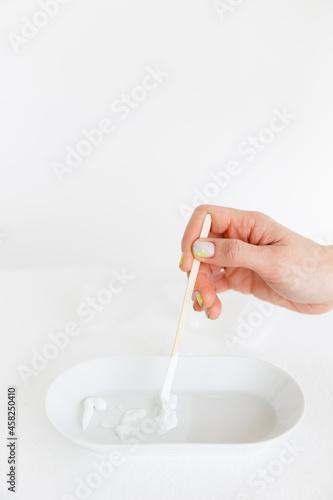 a wooden stick is placed in an oval saucer with a cosmetic cream. there are several cream textures in a white saucer on a white background. Cosmetology and care.