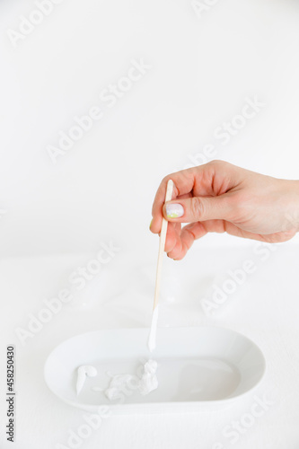 a wooden stick is placed in an oval saucer with a cosmetic cream. there are several cream textures in a white saucer on a white background. Cosmetology and care.