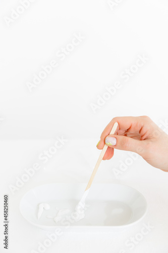 a wooden stick is placed in an oval saucer with a cosmetic cream. there are several cream textures in a white saucer on a white background. Cosmetology and care.