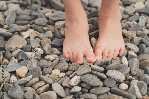 Prevention of flat feet in children. The child walks on the stones with his bare feet. Treatment of valgus foot in children and adults. Close-up of the child's foot on the rocks