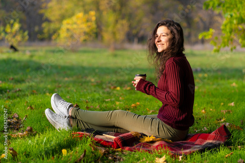 Pretty girl enjoys autumn and the beauty of nature sitting on a green lawn in the park. Autumn mood © Kate