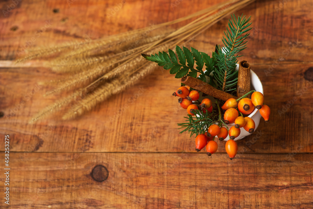 A composition with a cup with spruce branches, rosehips and spikelets of wheat on a wooden background A composition with a cup with spruce branches, rosehips and spikelets of wheat on a wooden background