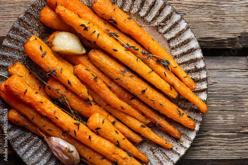 Healthy Homemade Roasted Carrots Ready to Eat. Glazed carrot with herbs and garlic top view. Fried carrot on wooden background. Sauteed vegetables. Comfort food.