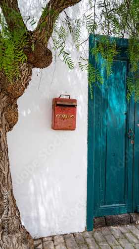 boite aux lettres rouge sur mur blanc à coté d'une porte bleue et d'un arbre