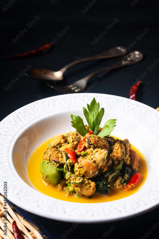 Thai Food concept Fried Mussels in yellow curry in white dish on black slate stone with copy space Thai Food concept Fried Mussels in yellow curry in white dish on black slate stone with copy space