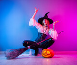 slender girl in a witch costume for Halloween with a broom and a pumpkin