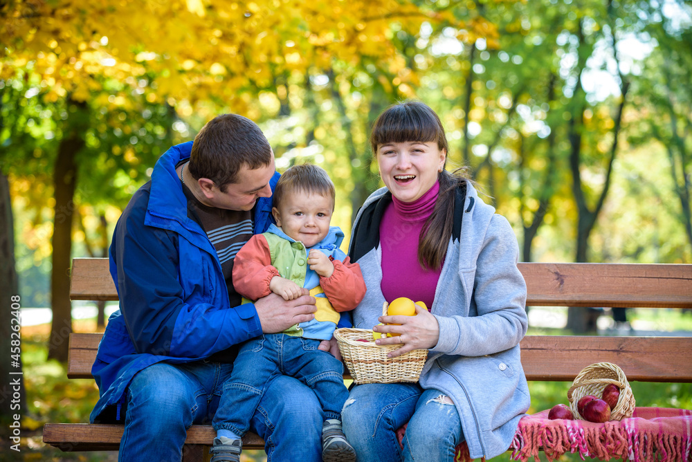 Fototapeta premium happy family enjoying autumn picnic. Father mother and son sit on bench with apples basket. Happy family leisure together concept