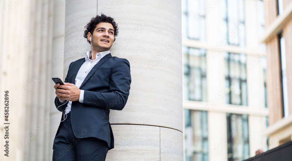 Communicates with clients by phone. The entrepreneur is standing near the office in the business center. A businessman goes to work in a business suit. Communicates with clients by phone. The entrepreneur is standing near the office in the business center. A businessman goes to work in a business suit.