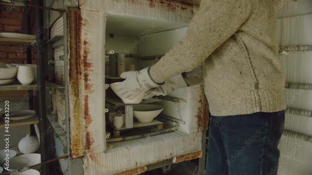 Young man ceramist is working in studio, removing dried items from the kiln, wearing gloves to take hot ceramics, concept of creative job and ceramics art, Slow motion. Young man ceramist is working in studio, removing dried items from the kiln, wearing gloves to take hot ceramics, concept of creative job and ceramics art, Slow motion.